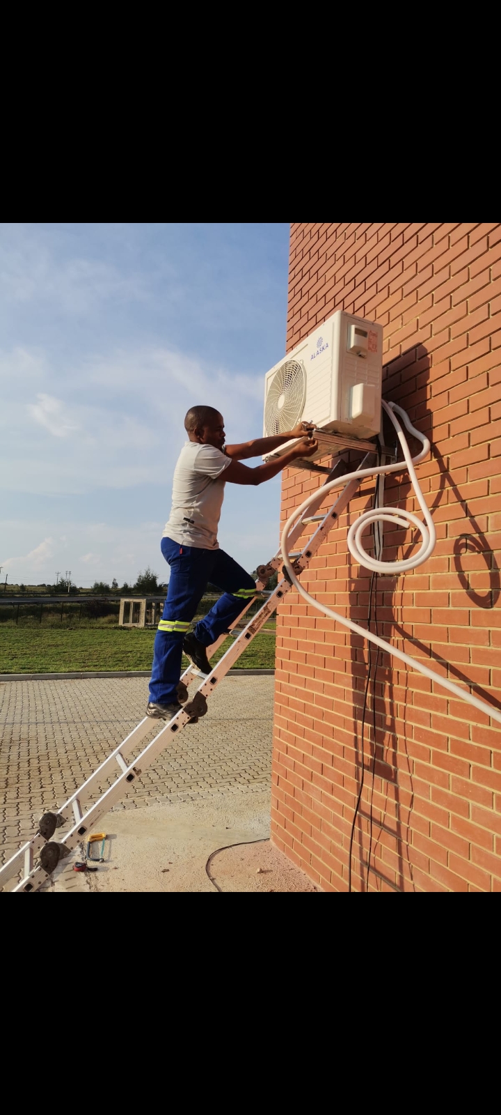 Technician servicing an outdoor air-conditioning unit on a ladder